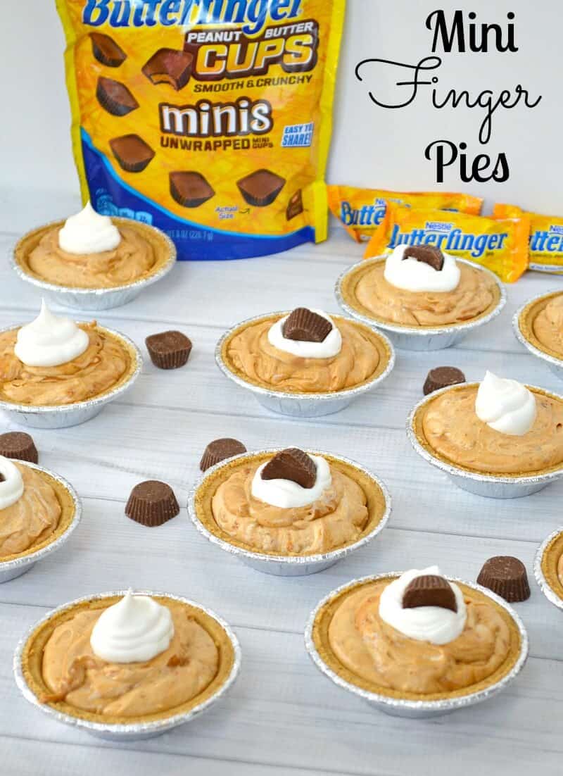 overhead view of small pies with light brown filling, small dollop of whipped cream topped with small piece of chocolate next to orange packaged candy bars on white wood table