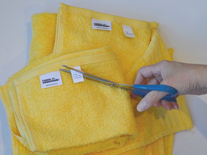 hand holding blue handled scissors cutting tags off of yellow towels