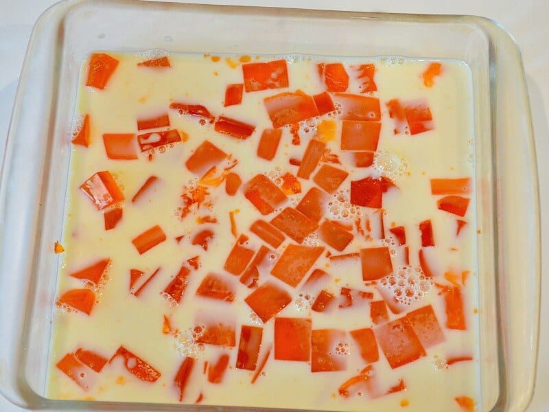 overhead view of square glass pan with cream colored liquid and orange cubes of gelatin scattered through