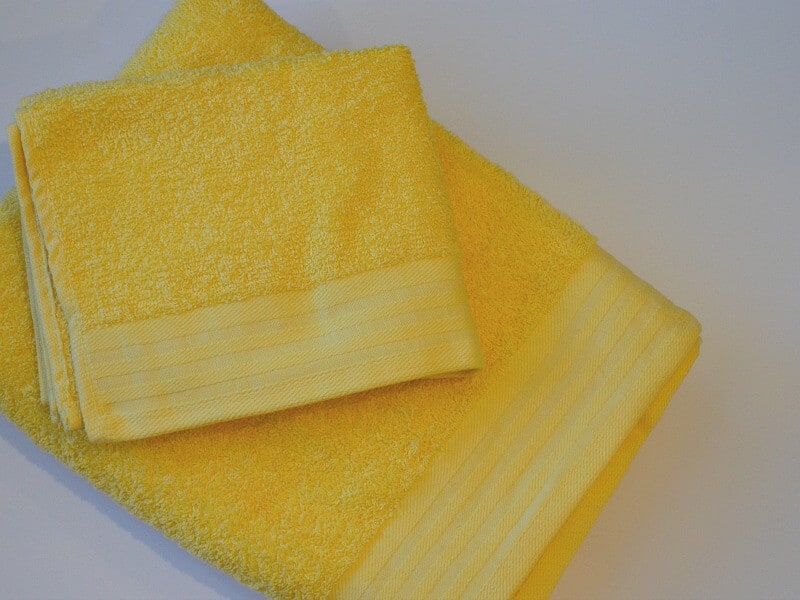 folded yellow washcloths on top of folded yellow towel on white table