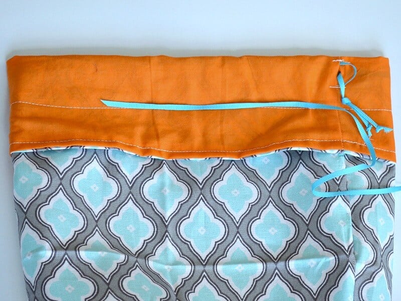 close up of threading blue ribbon into drawstring blue, grey and orange fabric bag 