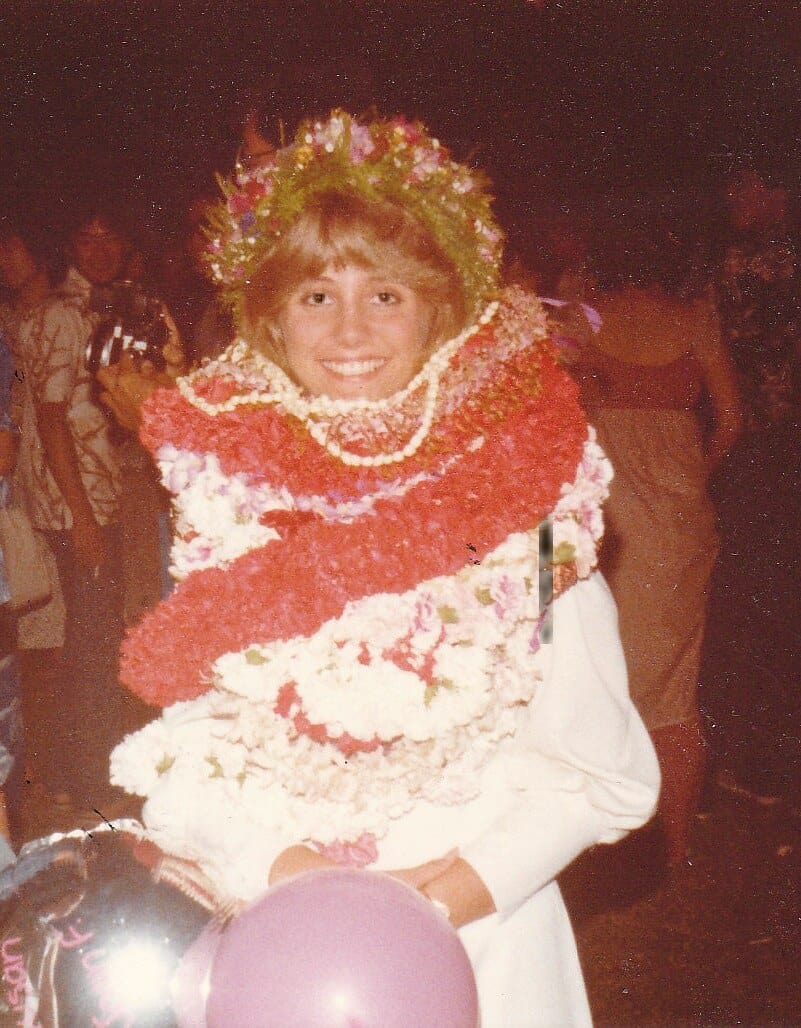 smiling girl wearing many leis with red lei on top