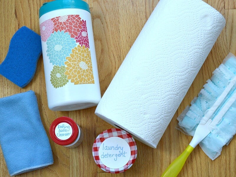 overhead view of blue sponge, blue cloth, white canister with floral label, 2 jars with handwritten labels, roll of paper towels and duster with yellow handle