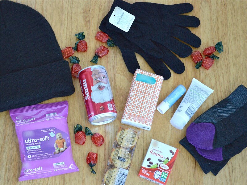 overhead view of red can of soda, hat and gloves with tag, small packet of tissues, package of crackers, box of raisins and black and purple socks
