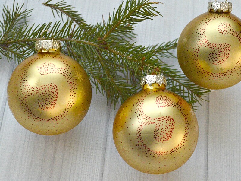 overhead view of 3 gold Christmas ball ornament with monogrammed letter "S" in red dots on pine branch