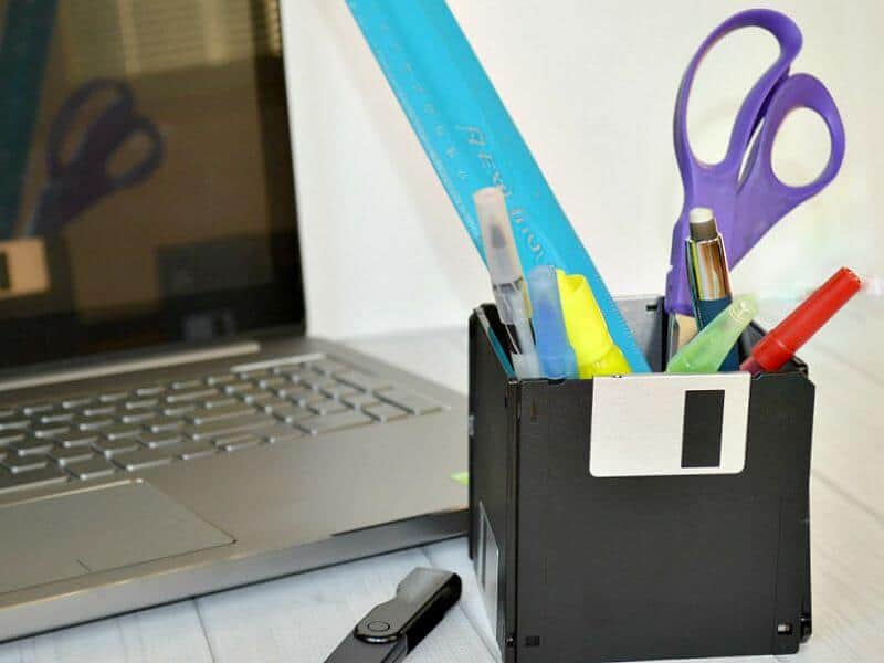 computer diskette holding pens, scissors and a ruler next to laptop computer