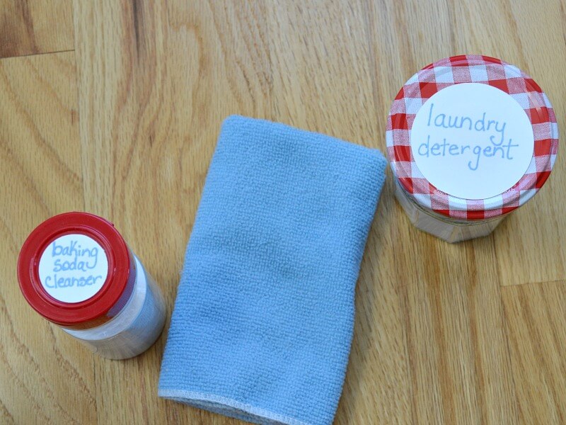 overhead view of blue cloth, bottle with red lid that says "baking soda cleanser" and glass jar with red and white lid that says "laundry detergent"