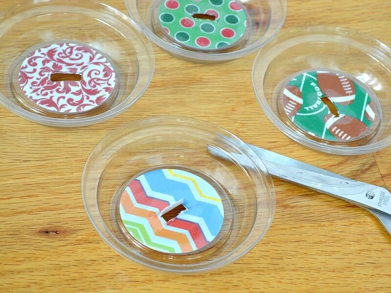 clear lids with circle of decorative paper and slit cut into middle of lid with pair of scissors nearby