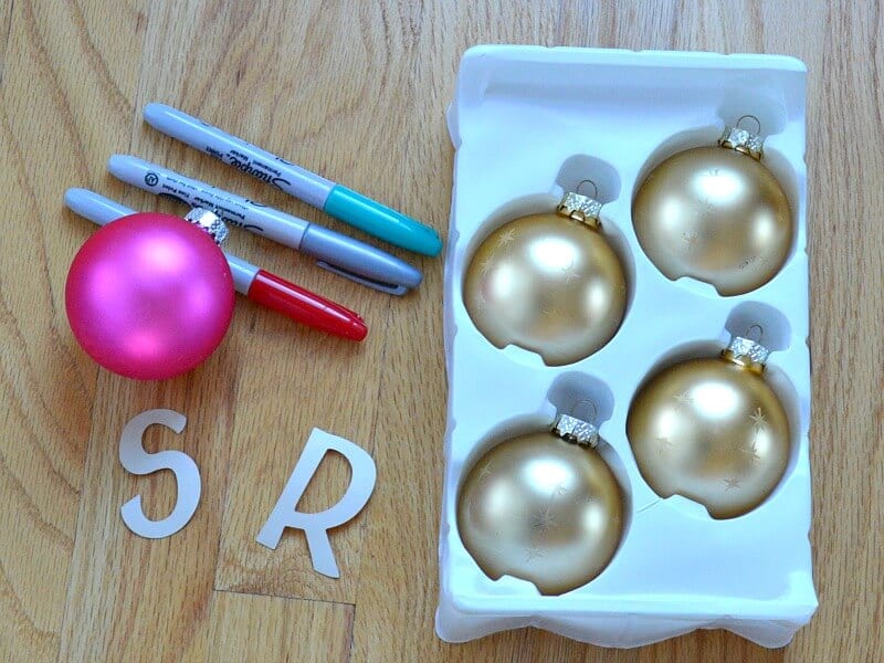 overhead view of 3 markers, a pink ball ornament, white stickers in S and R and a white tray with 4 gold ball ornaments
