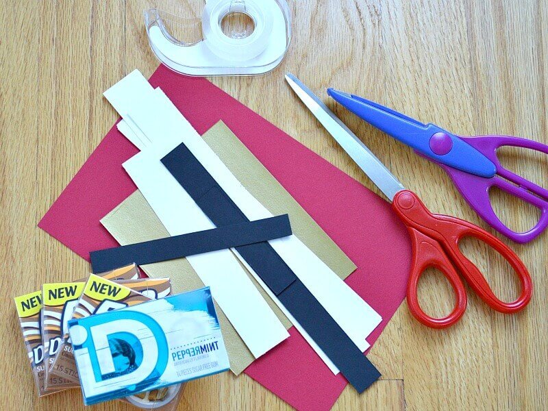 overhead view of red, white, and black strips of paper next to 2 pairs of scissors, roll of tape and 3 rectangular boxes of gum