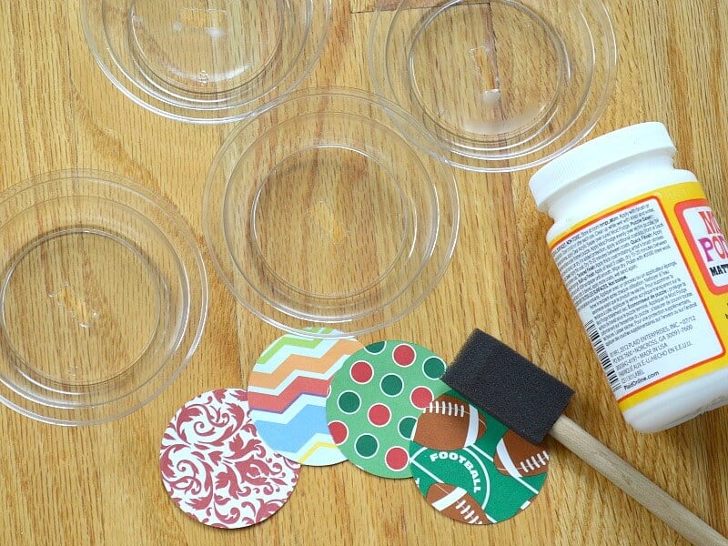 overhead view of clear lids, jar of glue, sponge brush and decorative paper cut into small circles