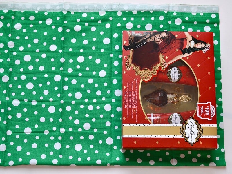 green fabric with white polka dots with red perfume box laying on top