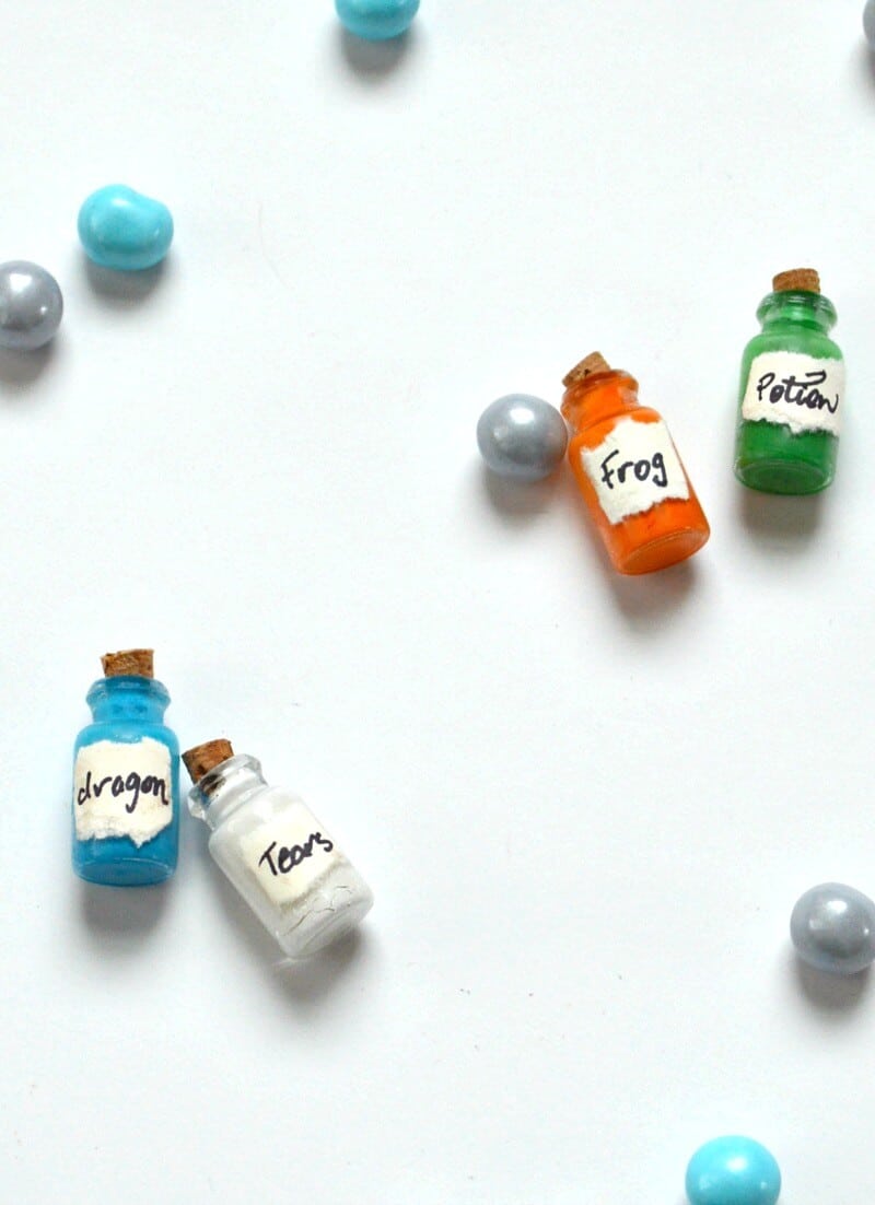 small colorful bottles with corks with blue, grey and white marbles scattered on white table