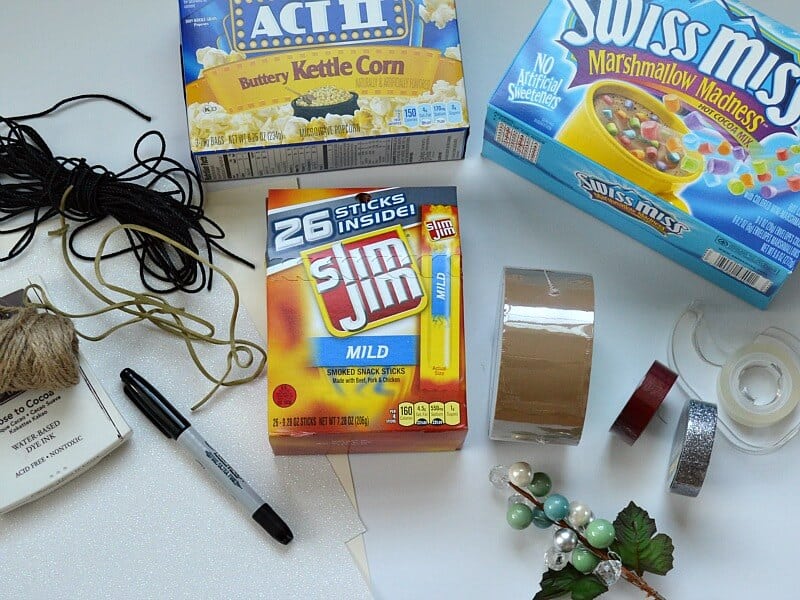 overhead view of box of microwave popcorn, box of hot chocolate mix and box of Slim Jims with craft supplies and tape scattered around