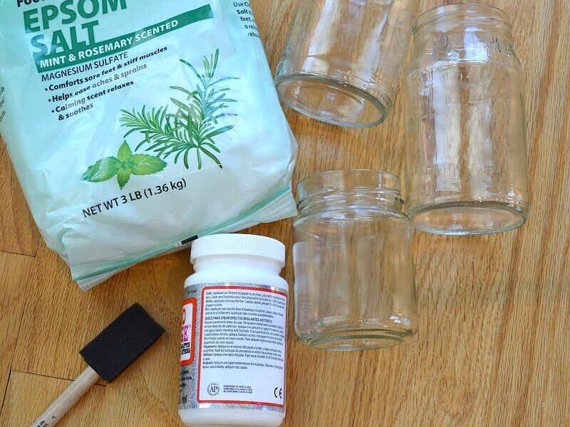 3 glass jars, bag of epsom salts, bottle of glue and sponge brush on wood table