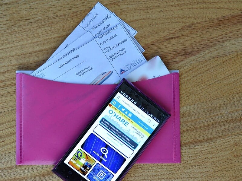 overhead view of pink envelope with airline tickets sticking out and cell phone with O'Hare airport website