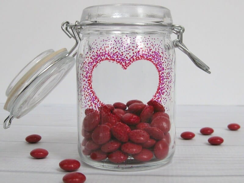 close up of heart on jar with red candy and candy scattered on table