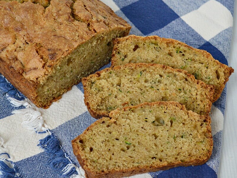 overhead view of loaf of zucchini bread and slices on blue checked table cloth