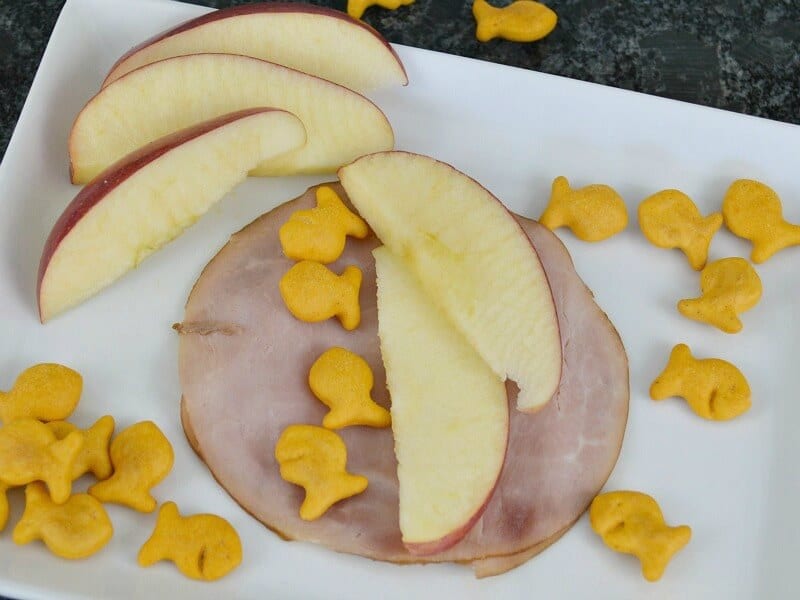 apple slices with fish crackers on piece of ham on white plate
