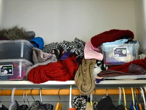 messy stack of scarves and tubs on closet shelf
