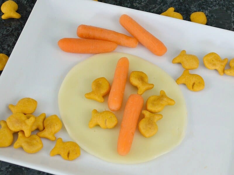 baby carrot sticks and fish crackers on piece of cheese on white plate