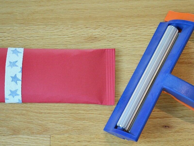 DIY firecracker candy wrapper with crimped edge laying next to paper crimper.