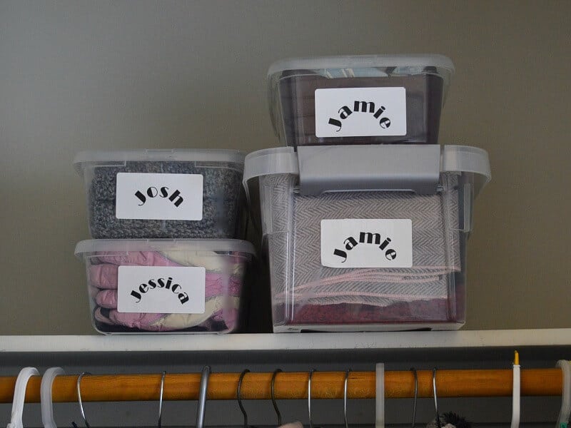 4 plastic tubs with labels stacked on closet shelf