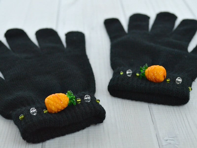 close up of pineapple beads on wrist of pair of black knit gloves on white table