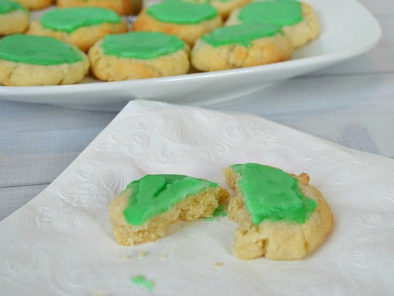 green frosted cookie on napkin in front of tray of cookies.