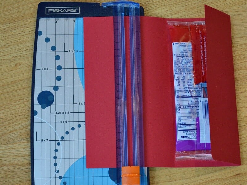 red paper measured out around package of candy and laying on top of paper cutter.