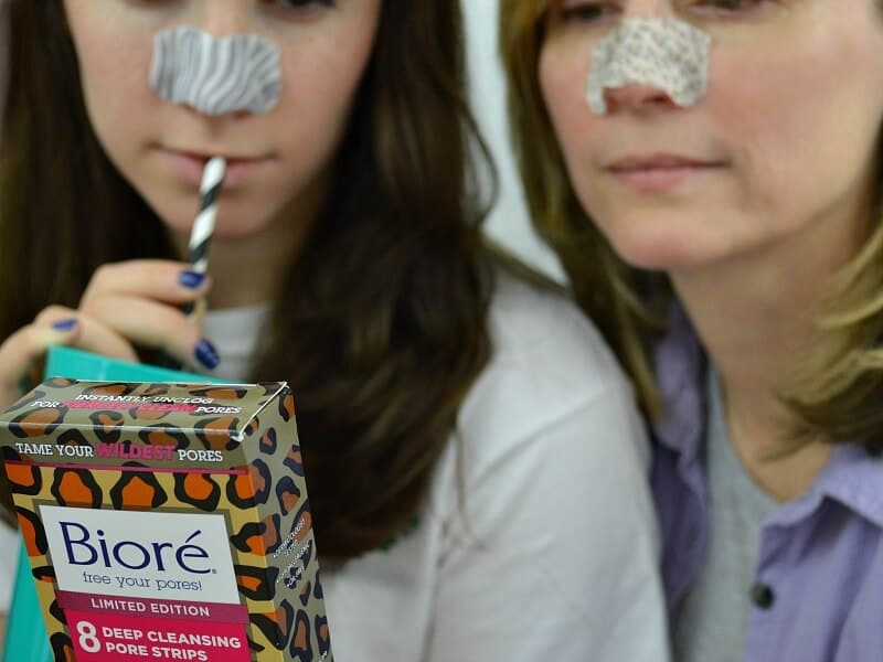 2 women wearing pore strips and reading back of box of product