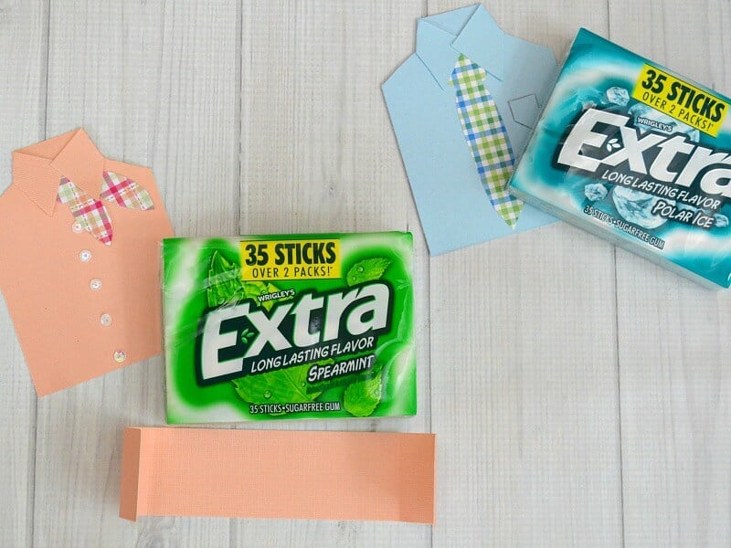 2 packs of gum laying next to paper crafted button shirts the size of the gum packs