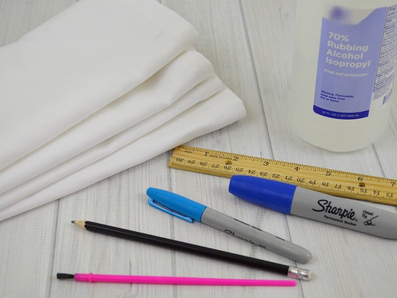 stack of white napkins, ruler, blue permanent markers, paint brushes and bottle of rubbing alcohol