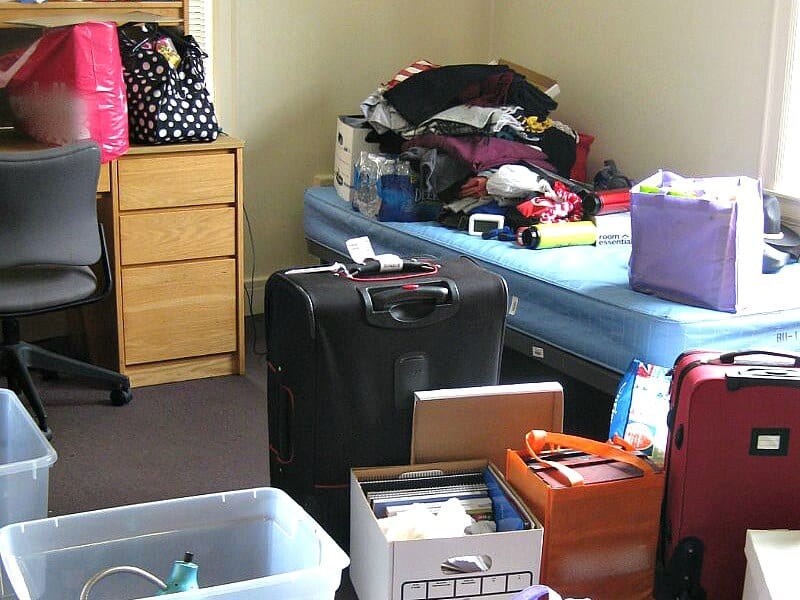 college dorm rom with suitcases, boxes and piles of items on move-in day