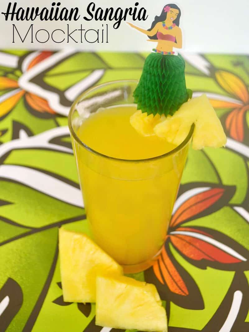 glass of yellow drink with pineapple and hula girl spike on tropical tablecloth