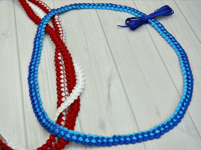 Dark and light blue ribbon lei lying on top of 3 red and white leis