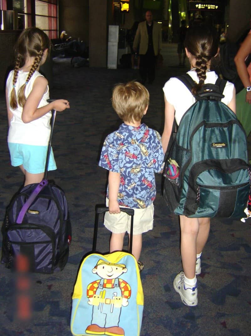 3 young children with backpacks walking through airport