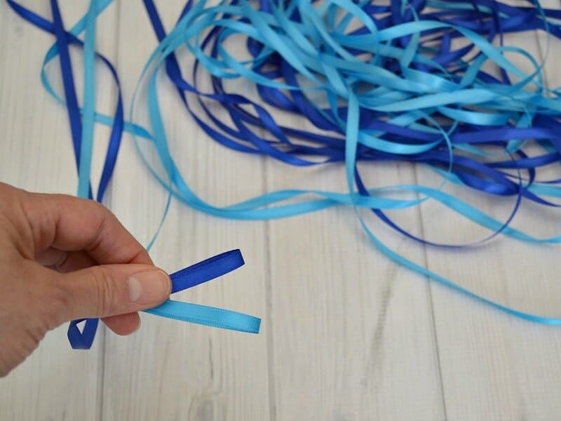 Pile of dark blue and light blue ribbon with hand holding two ribbons.