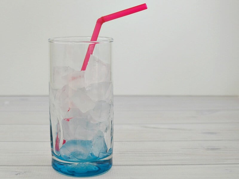 glass with ice and water and red straw on white wood table