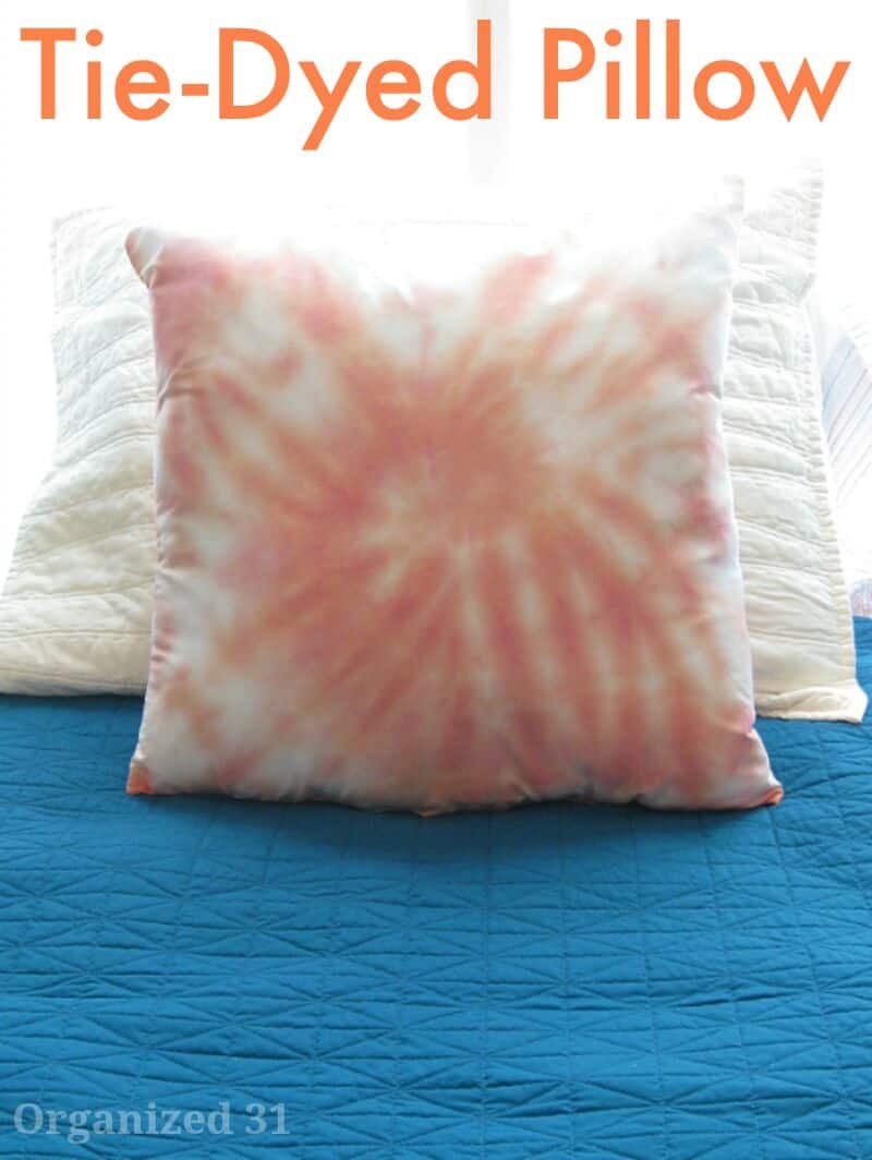 orange tie dye pillow on white pillow on blue bedspread