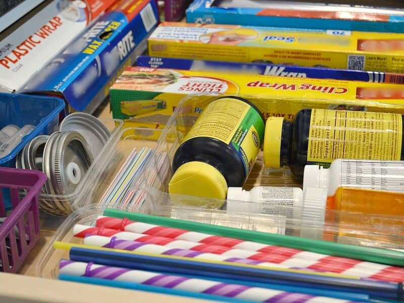 Side view of an organized kitchen drawer with boxes of food wrap, bottles of vitamins and straws