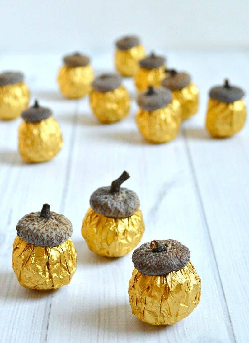 multiple DIY gold foil candy acorns on white wood table