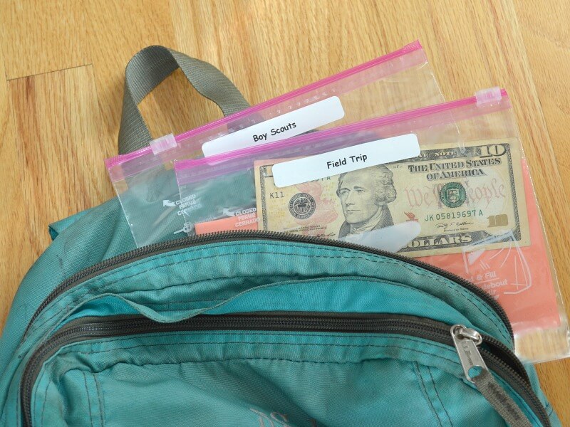 green backpack with plastic bags with labels saying "field trip" and "boy scouts"