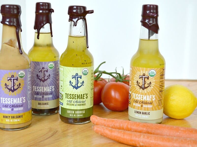 four bottles of dressing on wood table with lemons, tomatoes and carrots