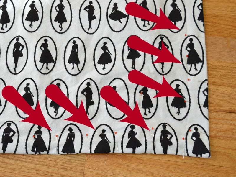 black and white fabric pinned together with red arrows pointing at the pins