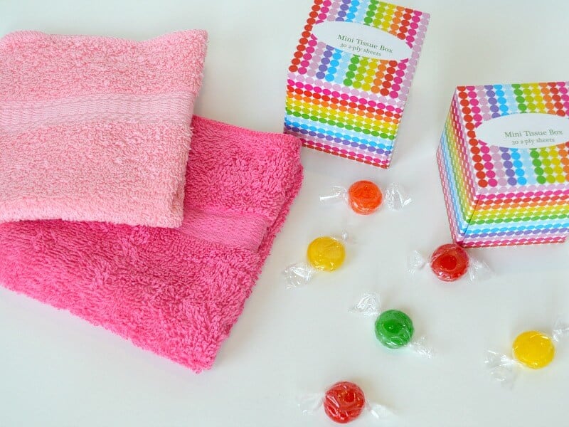 overhead view of colorful tissue boxes, washcloths and candy on white table