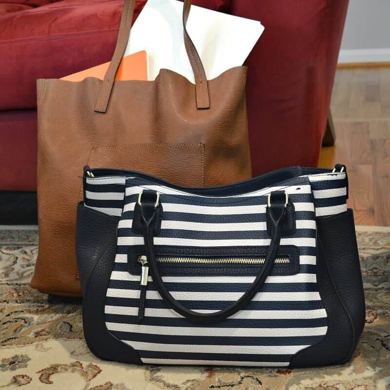 navy blue striped bag on rug in front of larger tan leather bag filled with books and paper