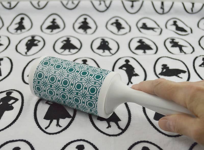 hand holding lint roller on top of blanket with fashion model motif