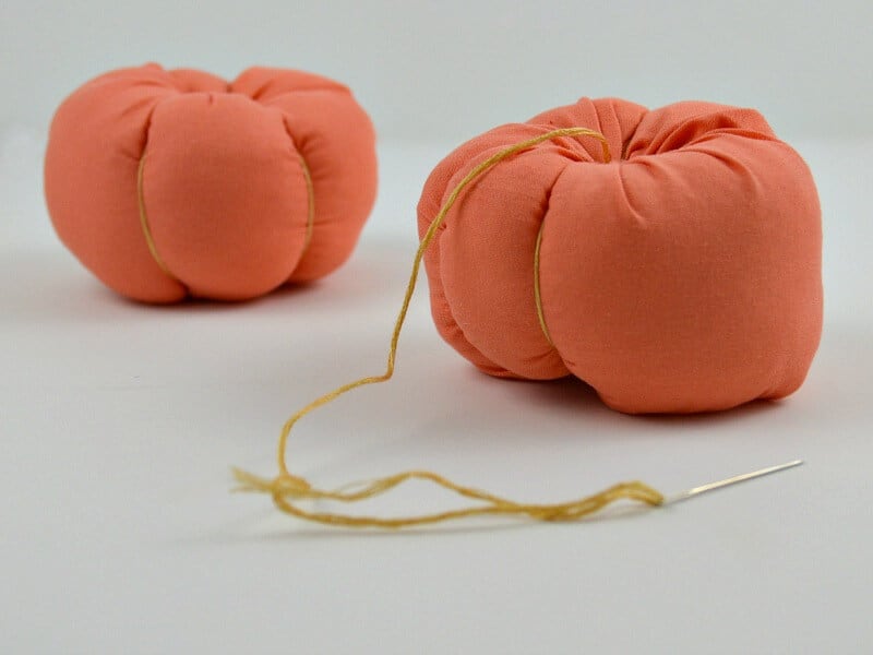 close up of 2 stuffed orange fabric pumpkins with needle and yellow thread