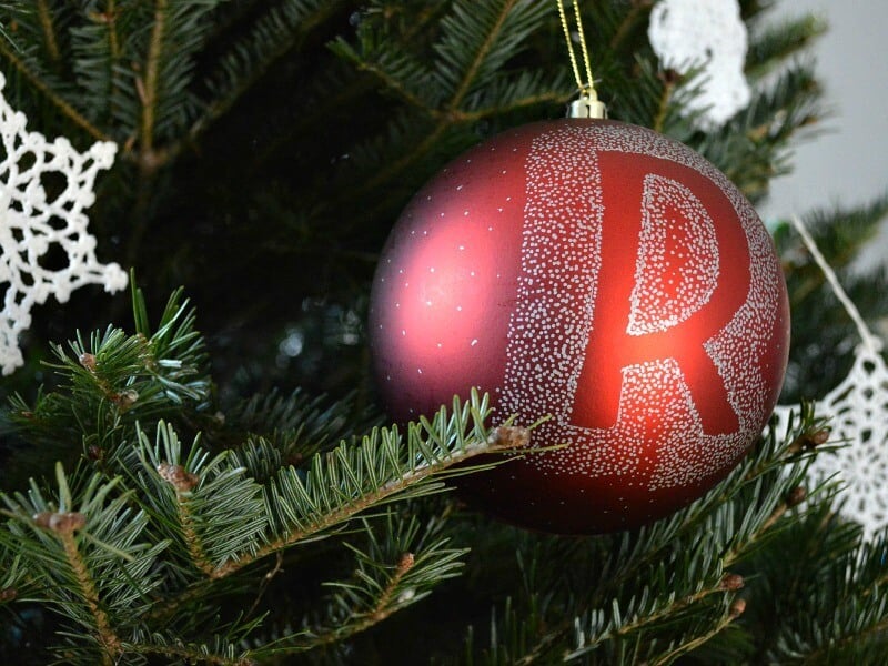 close up of monogrammed red Christmas ball on green pine tree with white snowflake ornaments